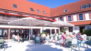 An outdoor café with tables and chairs, a building with red-tiled roofs, and a balcony with red flowers. - Hotel Frauensteiner Hof (Frauenstein)