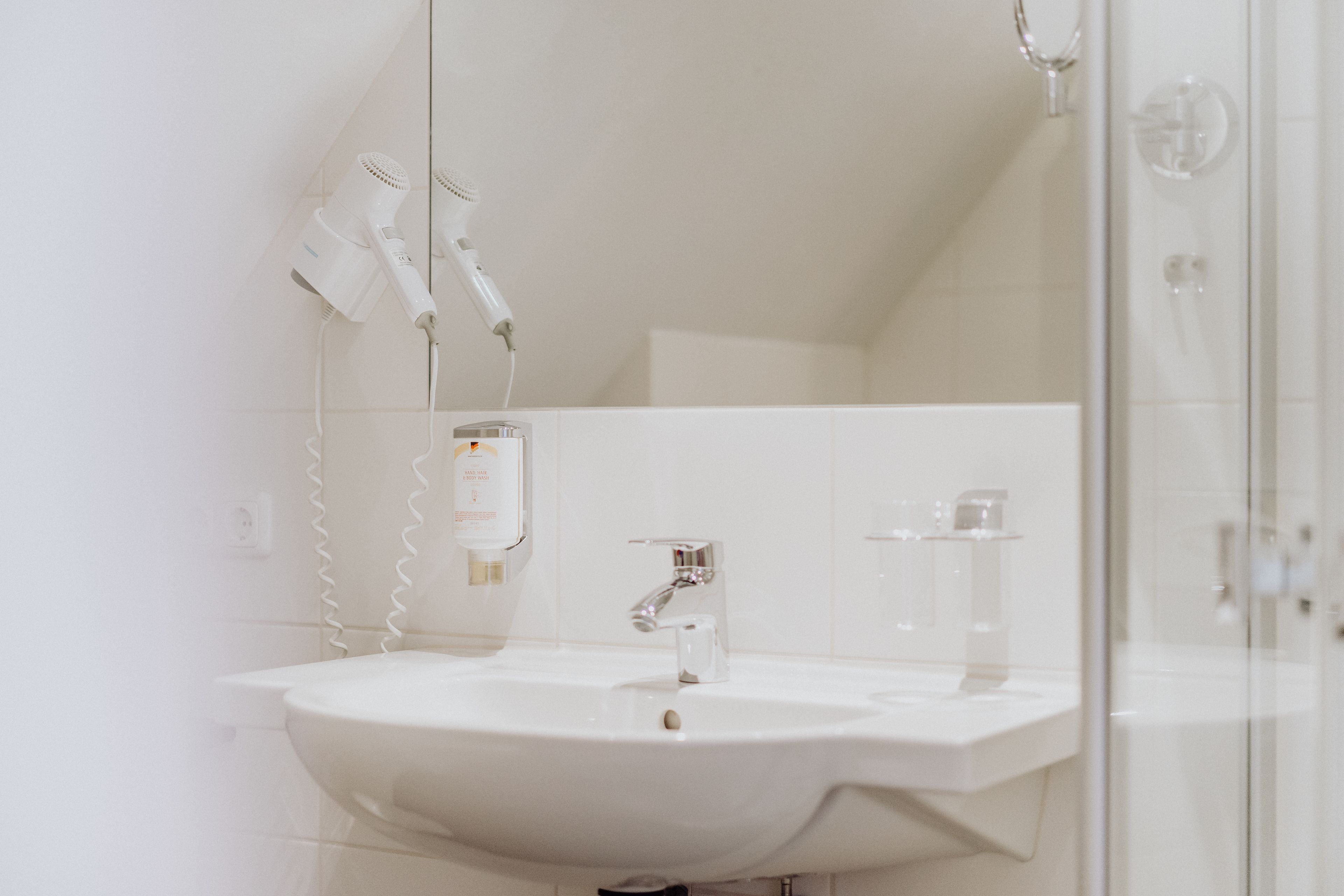Un baño con un lavamanos blanco, un espejo y dos secadores de pelo fijados en la pared.