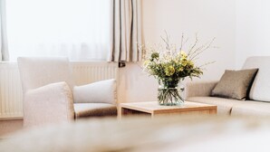 A living room with a beige sofa, a wooden coffee table with a vase of flowers, and a radiator in the background. - Hotel Frauensteiner Hof (Frauenstein)