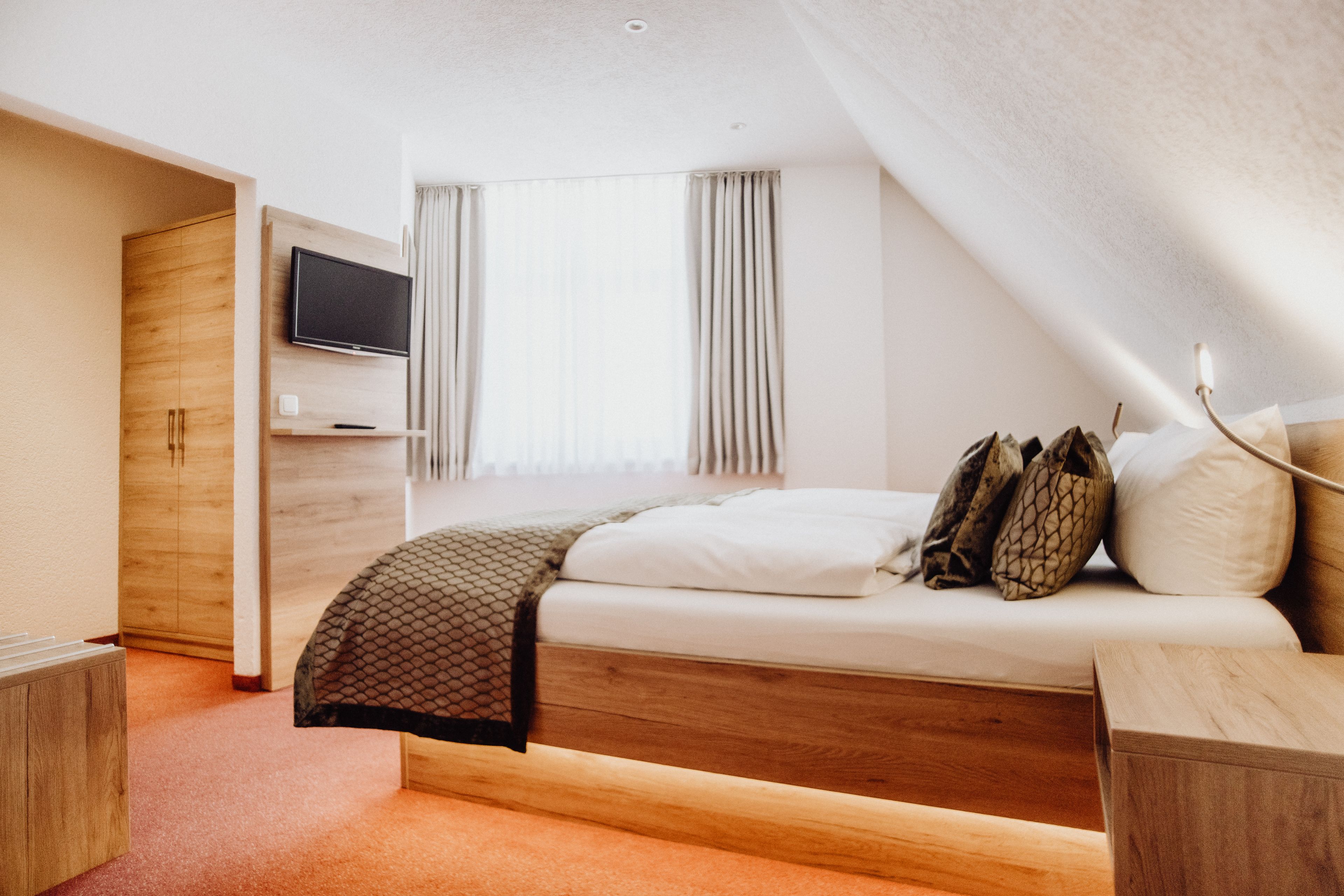 Une chambre moderne avec un lit en bois, un téléviseur fixé au mur et une fenêtre avec des rideaux.