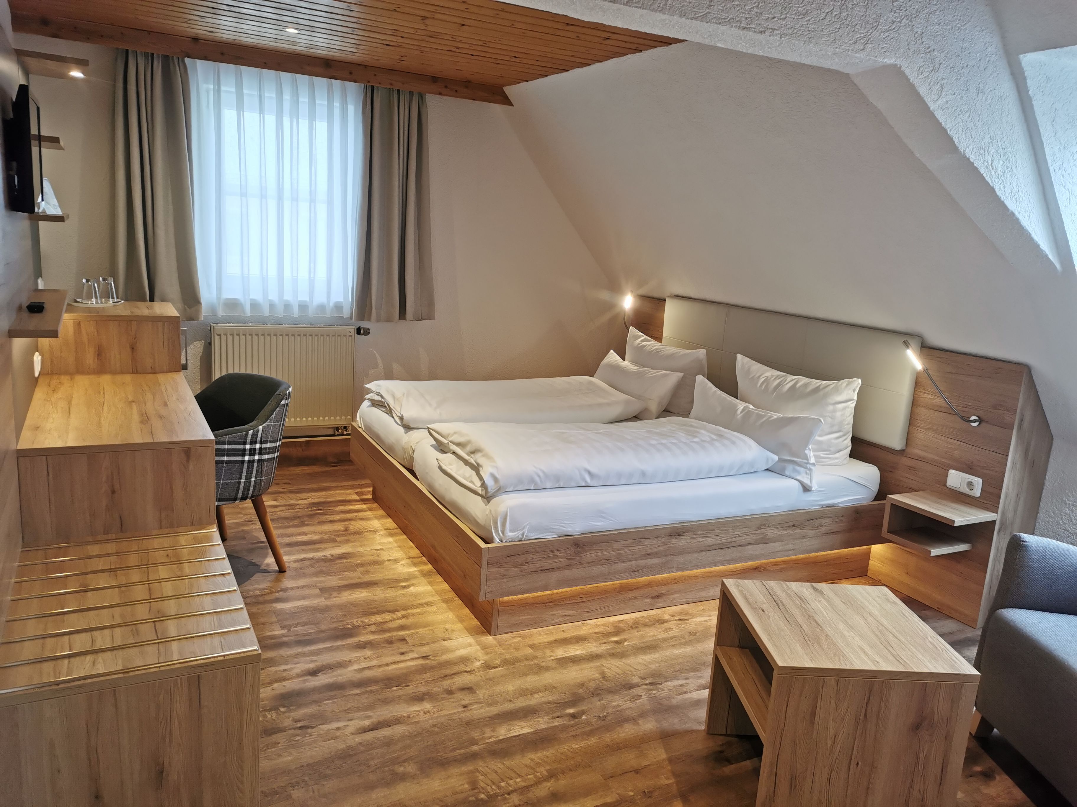 Un dormitorio moderno con cama de madera, mesitas de noche, una silla y un escritorio.