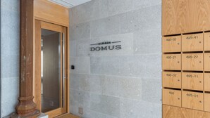 A hotel entrance with a stone wall, a wooden door, and a row of numbered wooden mailboxes. - Almada Domus (Porto)