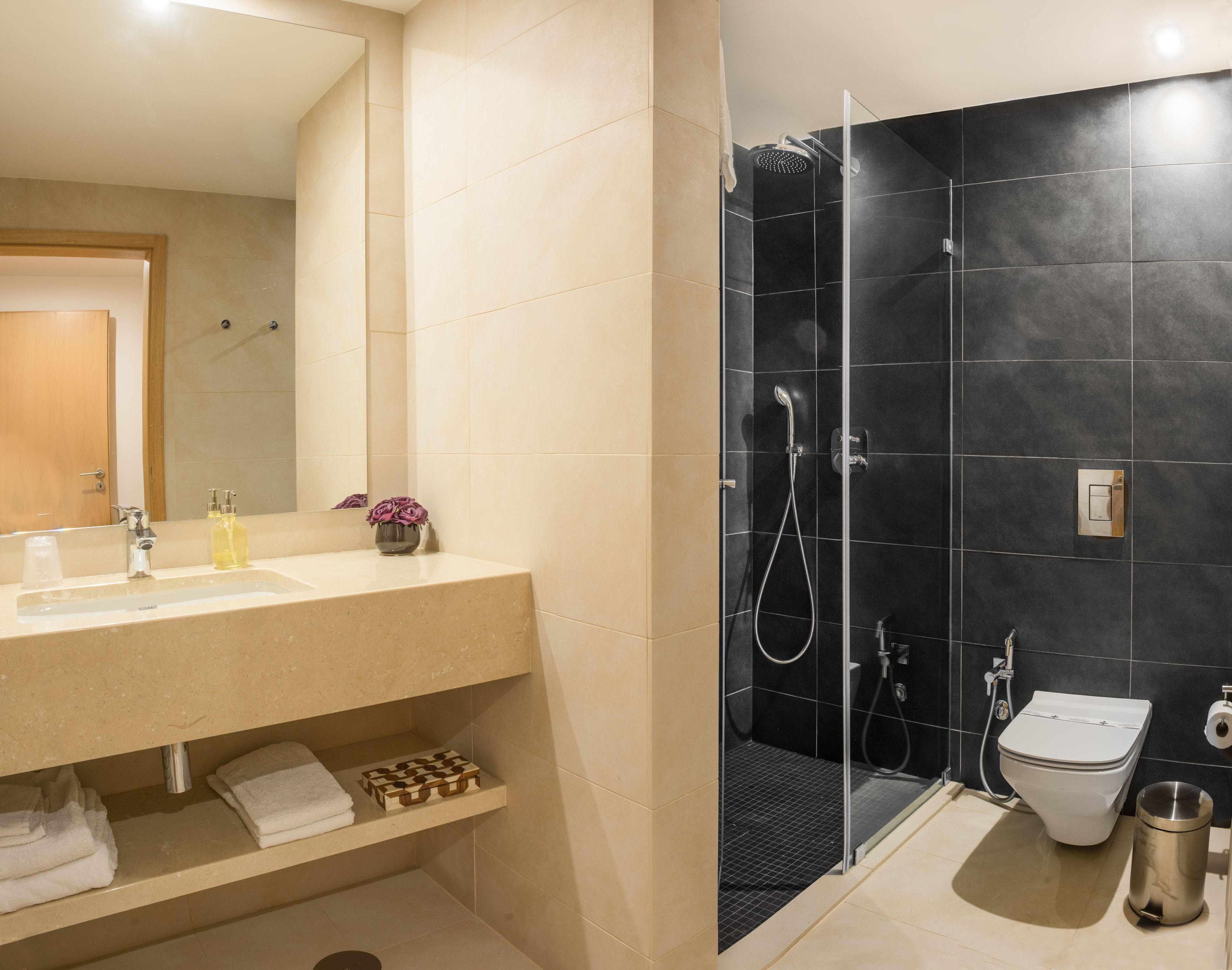 Un baño con un tocador color beige, cabina de ducha de vidrio, inodoro y un bote de basura.