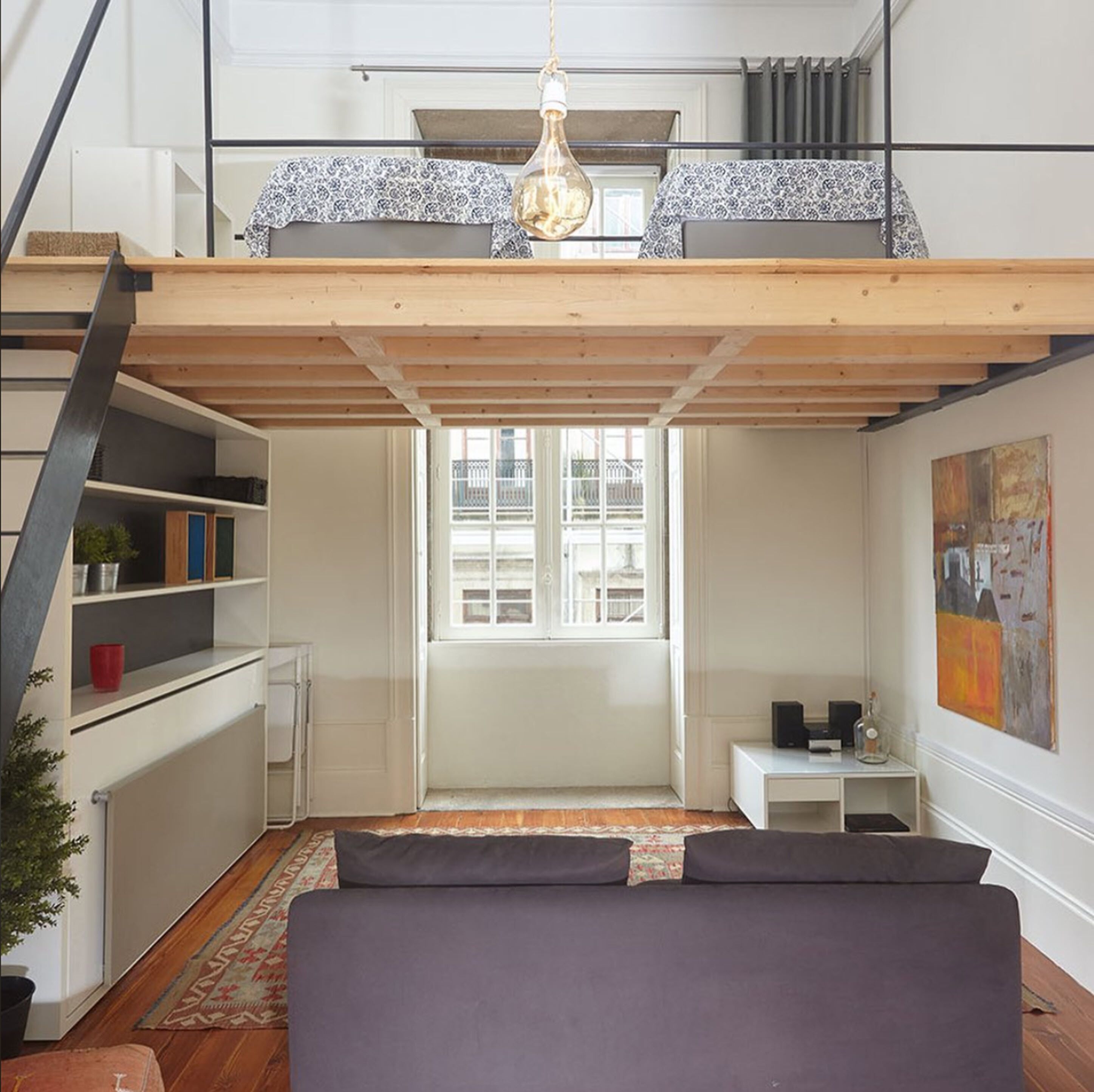 Een kamer in loftstijl met een bed, een bureau en een raam.