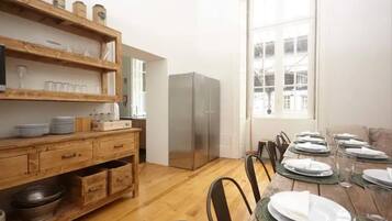 Un comedor con una mesa de madera dispuesta para cuatro personas, un refrigerador y un ventanal con vistas a edificios.