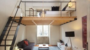 A loft-style apartment with a wooden floor, a sofa, a coffee table, a TV, and a staircase.