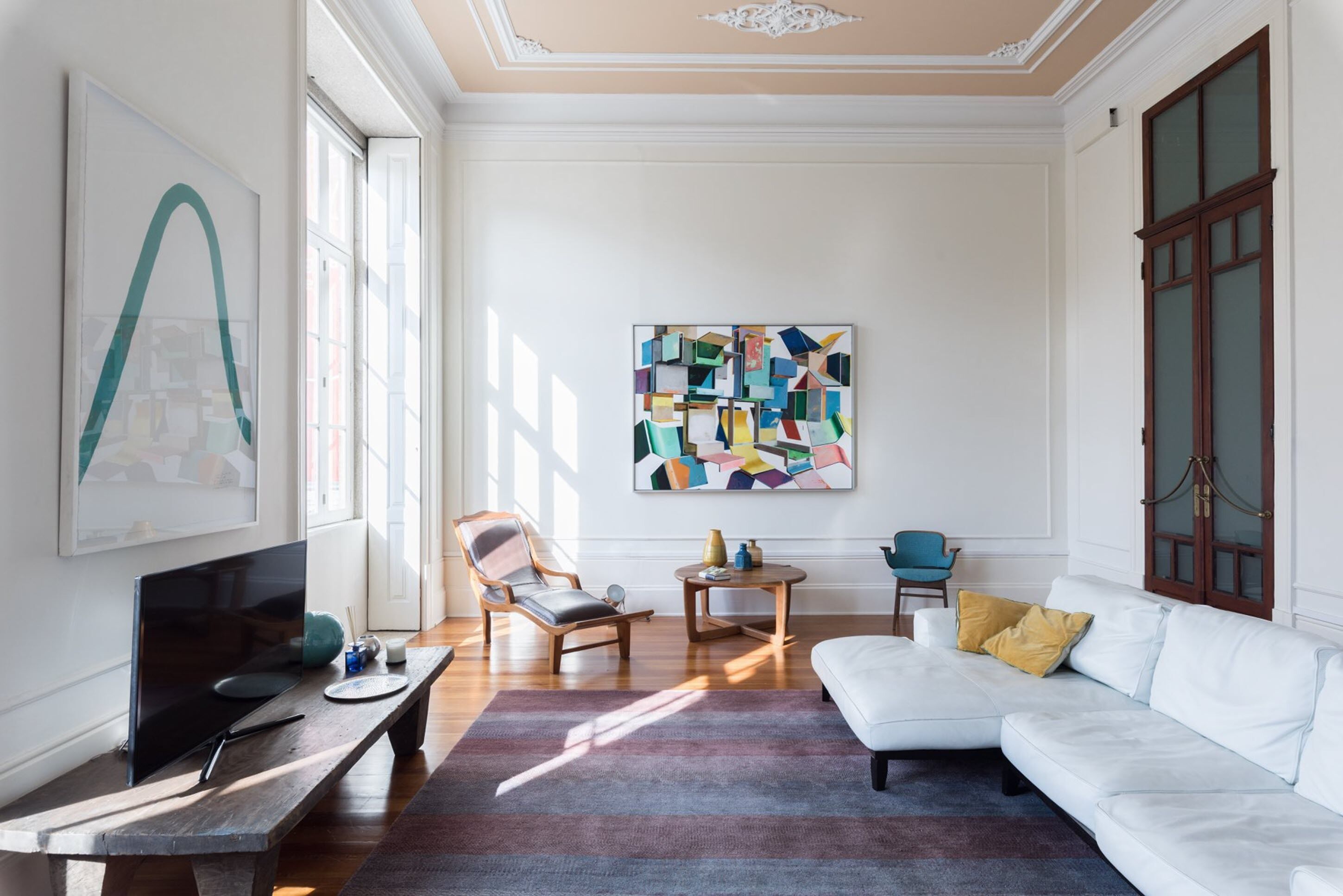Una sala de estar moderna con un sofá blanco, un televisor y un cuadro abstracto colorido en la pared.