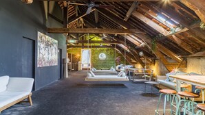 An interior with a high ceiling, exposed wooden beams, a seating area with a swing, and a bar with stools.
