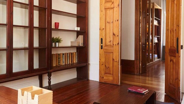 A room with a wooden bookshelf, a desk with a book, and a colorful rug.