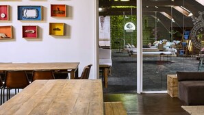 A modern hostel interior with a wooden dining table, a sofa, and a wall with small display cases.