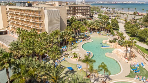 A resort with a large building, a pool area with lounge chairs, and a view of the sea. - Hotel Palas Pineda (Vila-Seca)