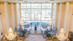 A grand lobby with large chandeliers, a central fountain, and a view of a pool through large windows. - Hotel Palas Pineda (Vila-Seca)