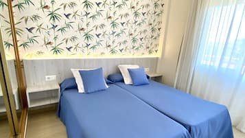 Ein Hotelzimmer mit zwei Betten, Bambusblatt-Tapete und einem großen Fenster mit Vorhängen.