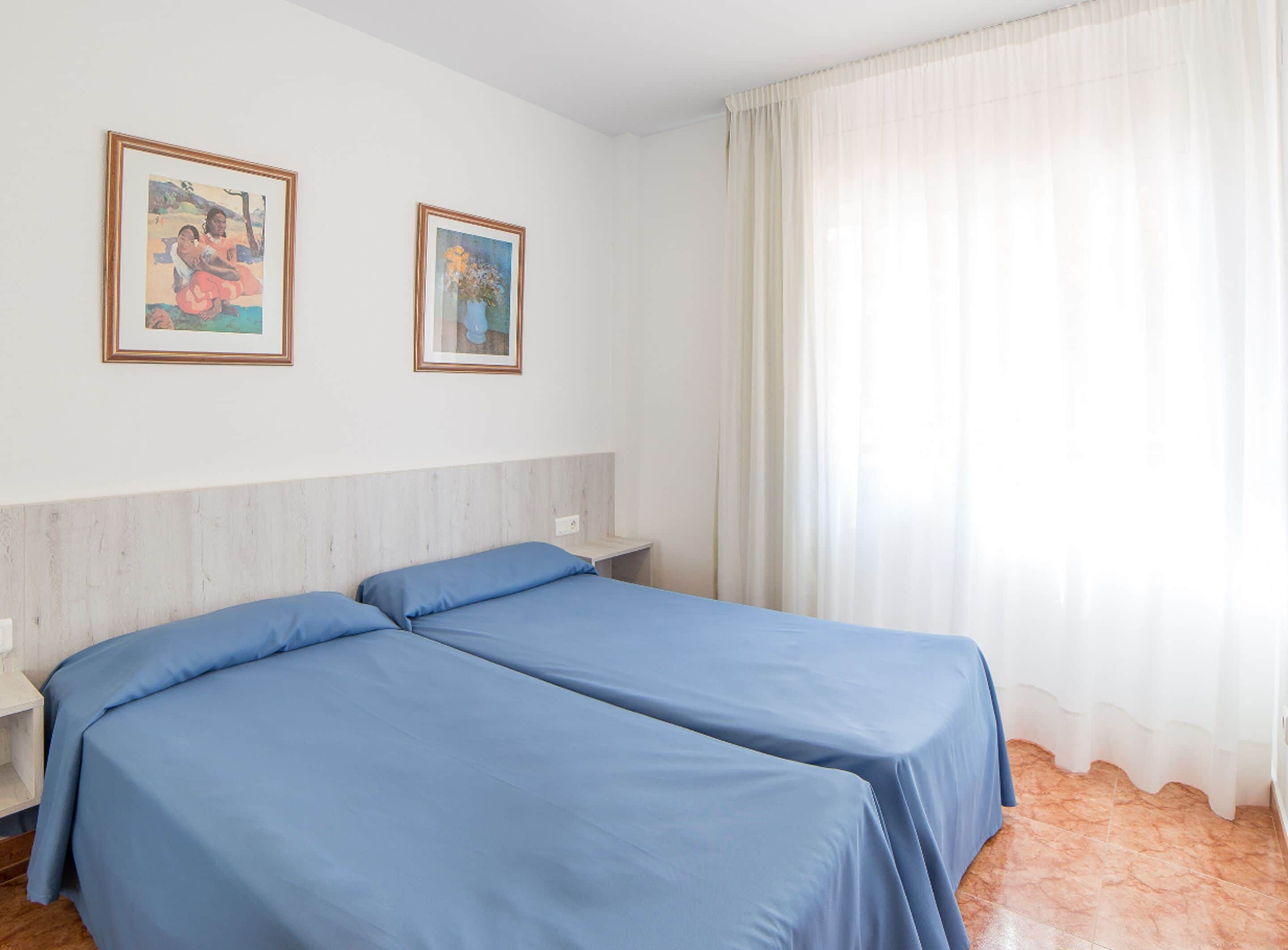 A room with two beds, a nightstand, and two framed pictures on the wall.