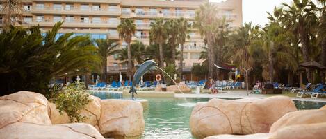 A hotel pool area with large rocks, palm trees, and a dolphin statue.