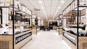 A modern cafe with wooden shelves and tables, featuring a variety of food items and beverages. - Hotel Palas Pineda (Vila-Seca)