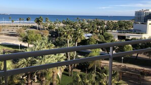 A balcony with a view of a beach, palm trees, and a building with a sign that reads "TAURANT". - Hotel Palas Pineda (Vila-Seca)
