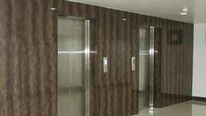 Dos puertas de ascensor en un pasillo con pared texturizada y suelo de baldosas.