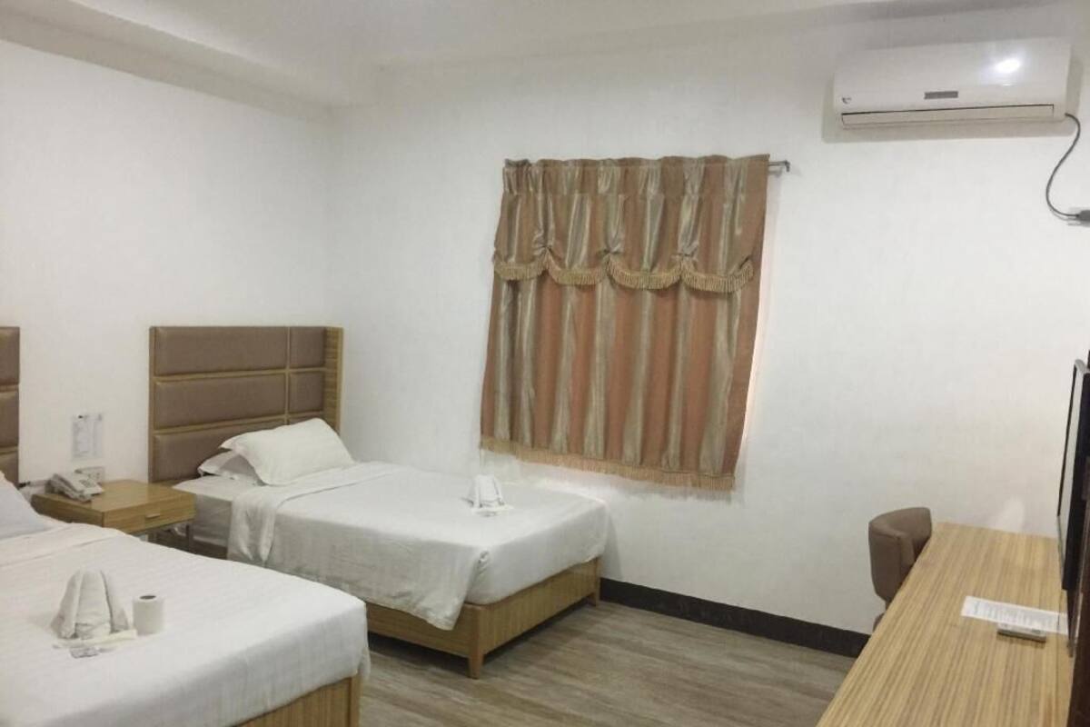 Een hotelkamer met twee bedden, een bureau en een raam met gordijnen.