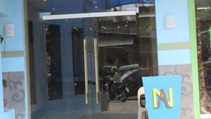Entrada de un edificio moderno con puertas de vidrio, una cámara de seguridad y un letrero azul con la letra 'N' en amarillo.