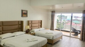 Habitación de hotel con dos camas, una mesita de noche con lámpara y vistas a edificios a través de un ventanal grande.