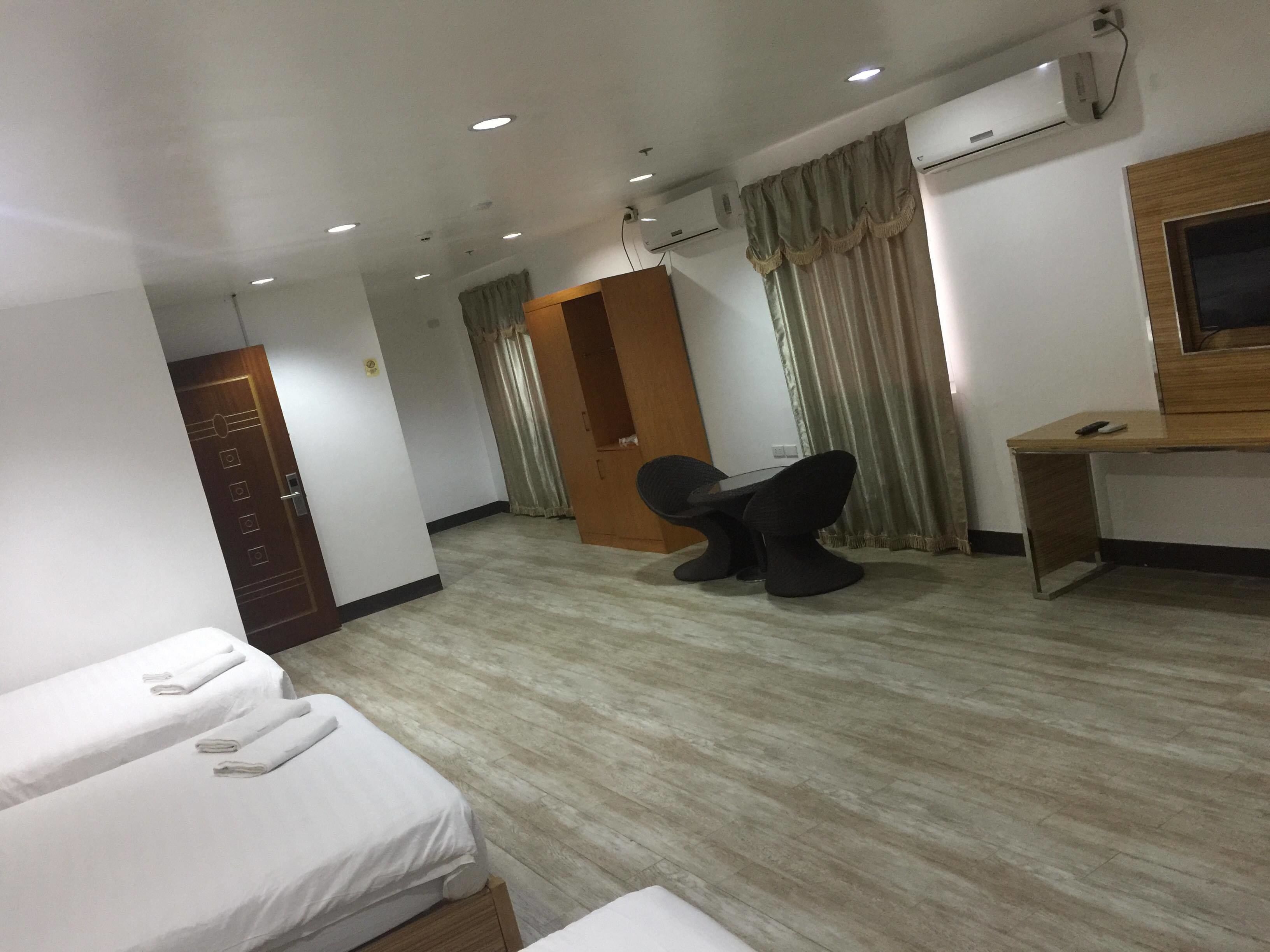 A hotel room with two beds, a desk, a chair, an air conditioning unit, and a television.