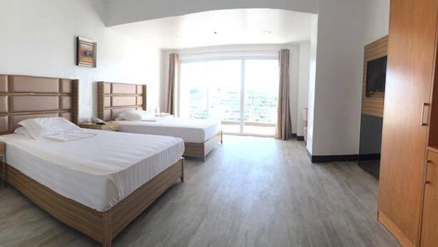 Una habitación de hotel con dos camas, un armario de madera, una mesita de noche y un ventanal con vistas.