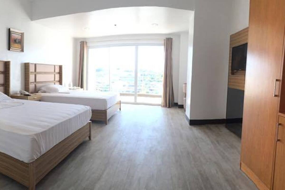Een hotelkamer met twee bedden, een houten kledingkast, een nachtkastje en een groot raam met uitzicht.