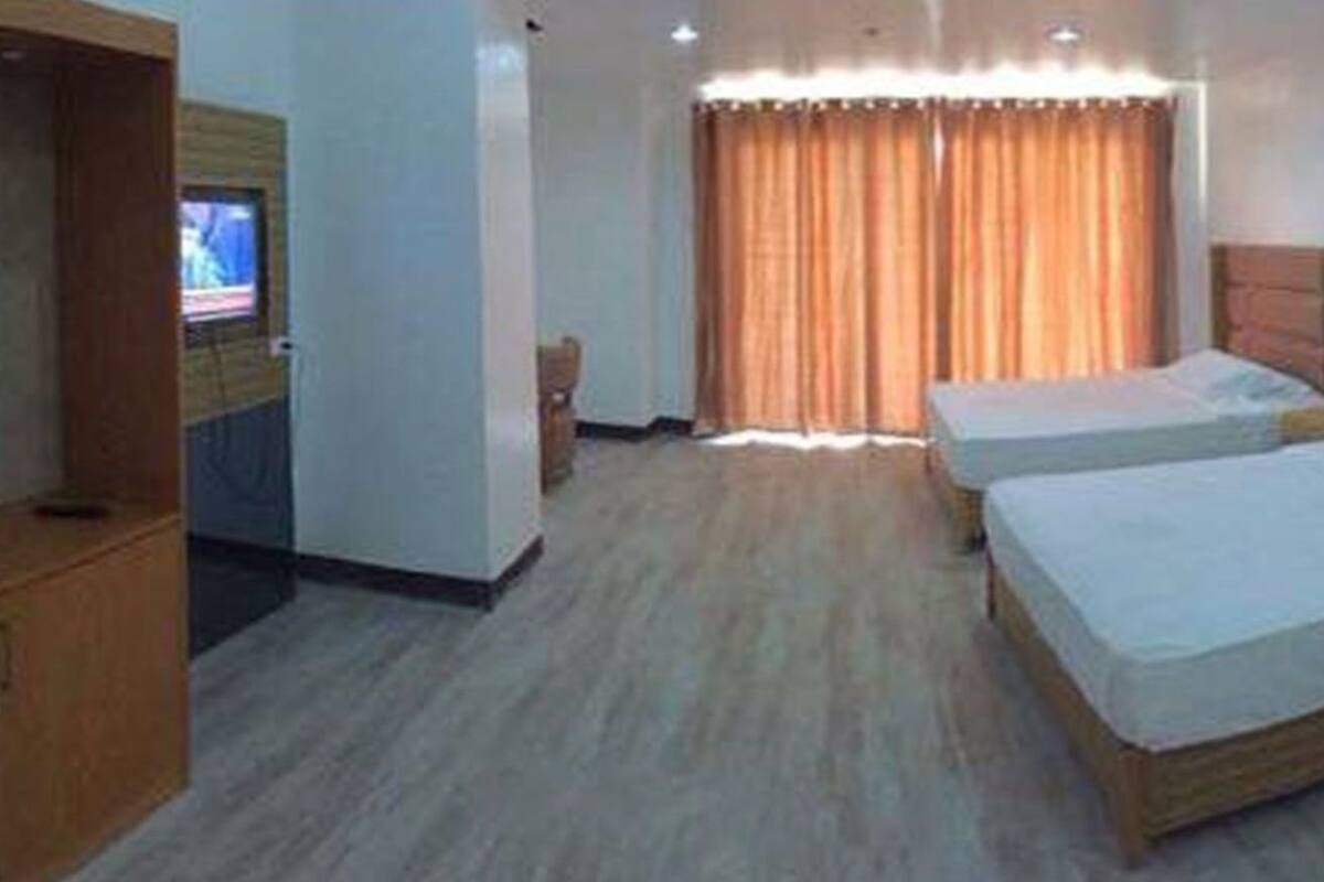 Een hotelkamer met twee bedden, een houten garderobe, een televisie en een groot raam met gordijnen.