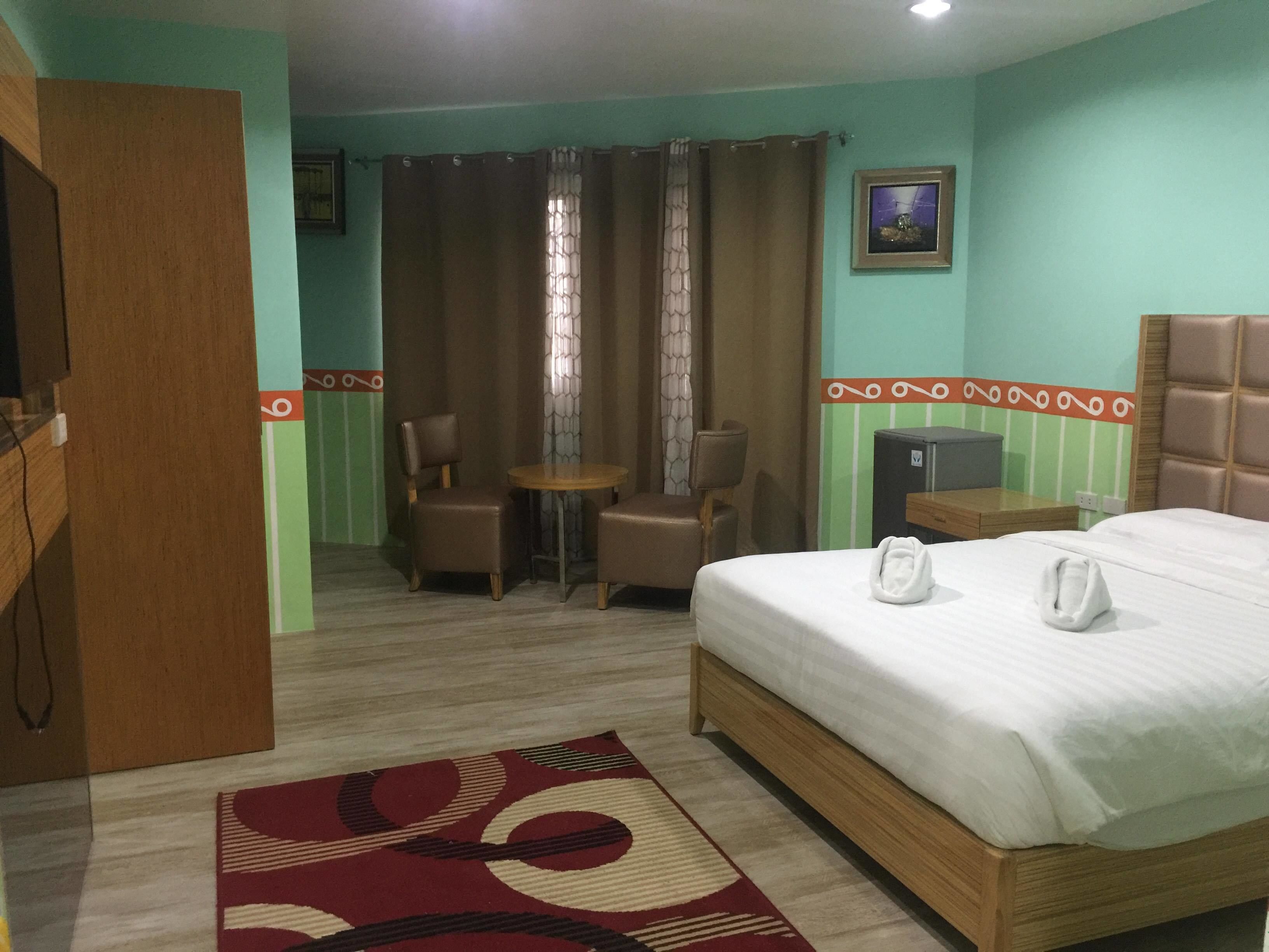 A hotel room with a bed, a desk, a chair, a small table, and a curtain.