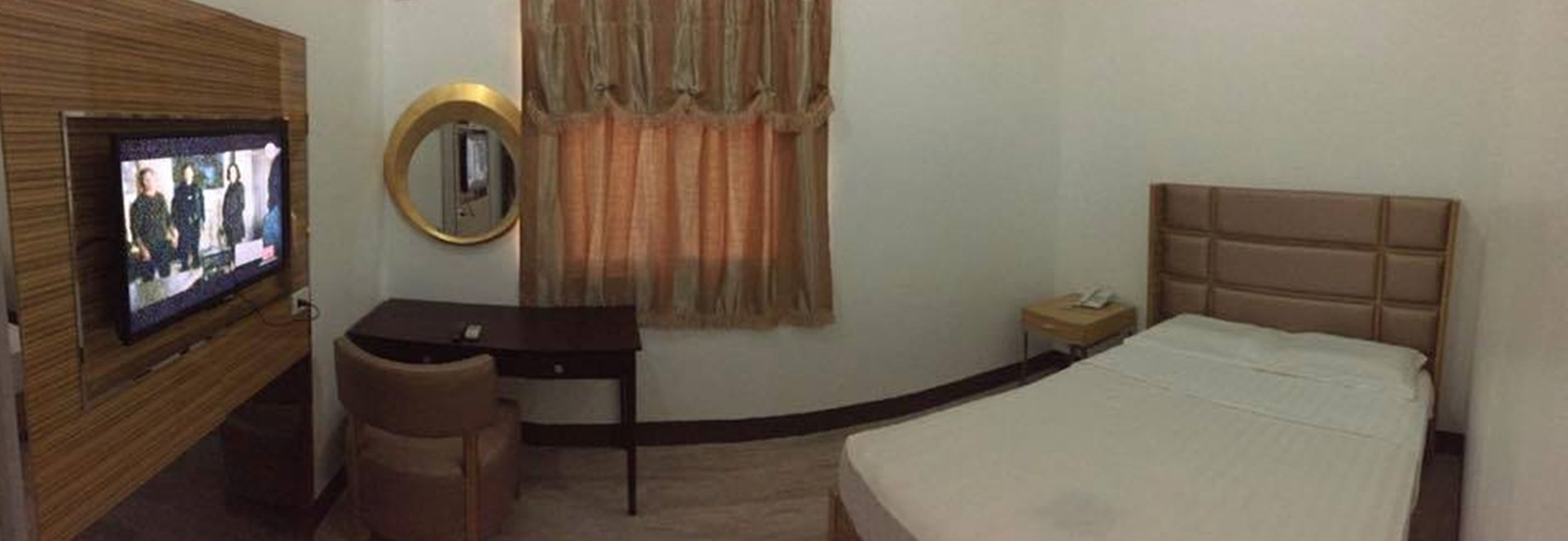 Ein Hotelzimmer mit Bett, Schreibtisch, Sessel, Fernseher und Spiegel.