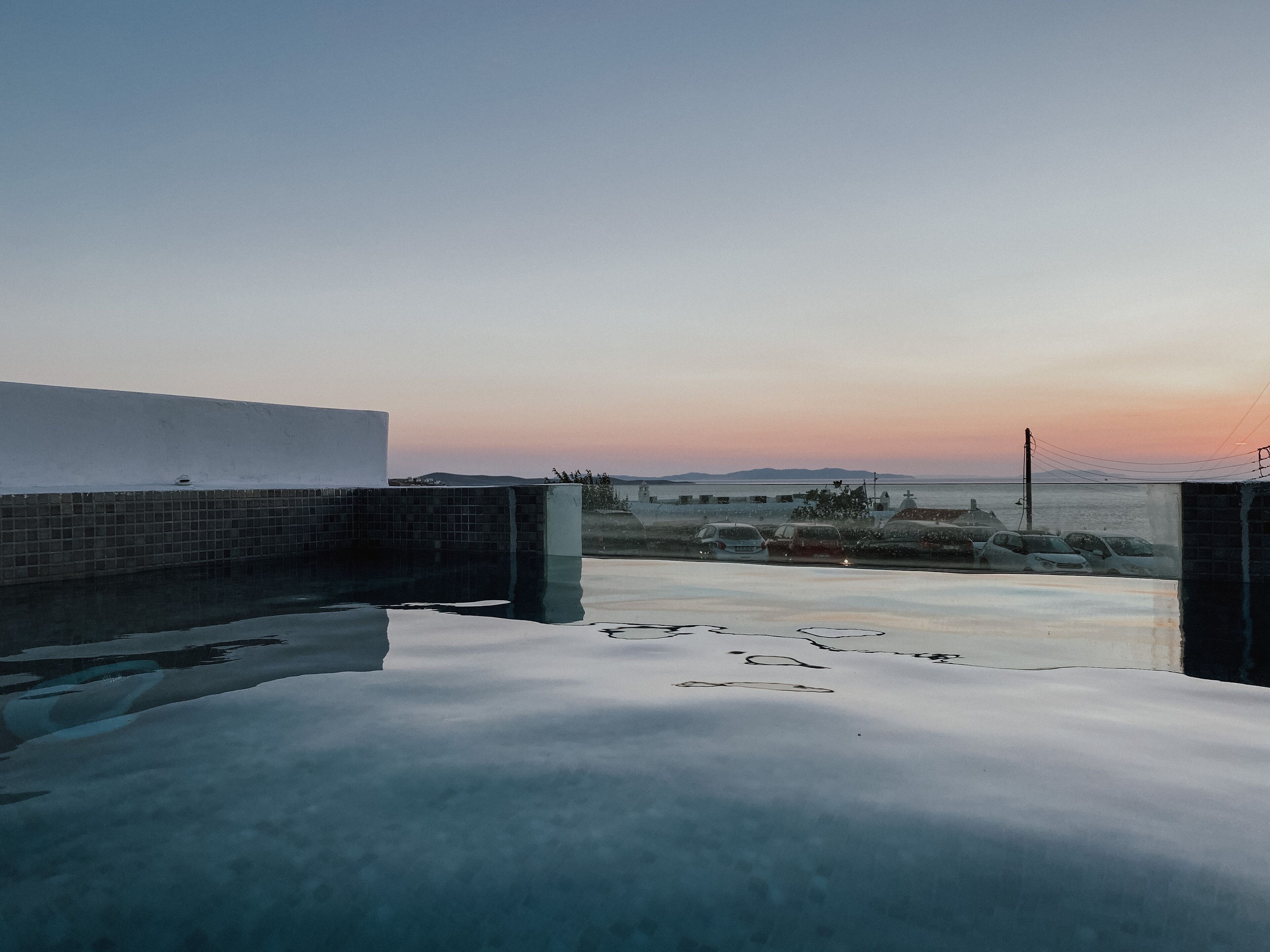 Una piscina en la azotea con vistas al mar y colinas lejanas al atardecer.