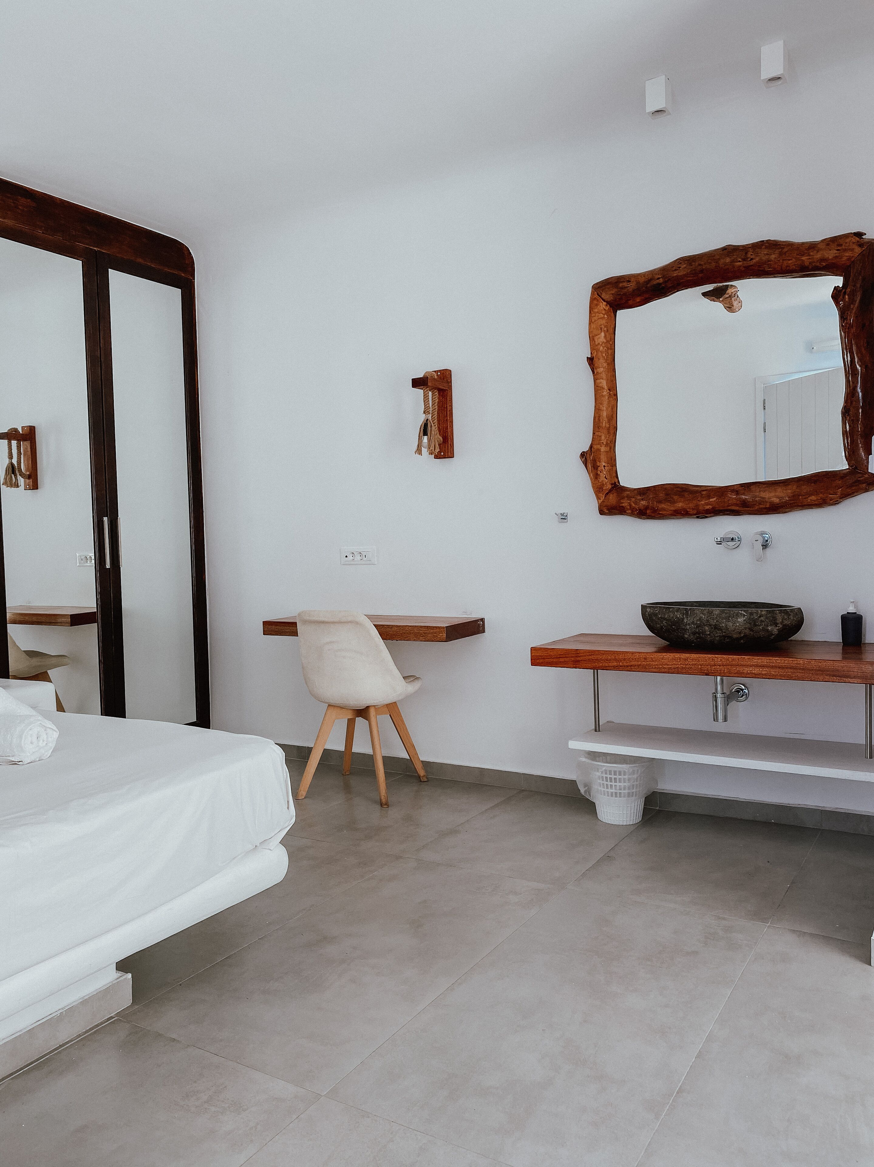 A modern bedroom with a bed, a chair, a wooden vanity with a mirror, and a small sink.