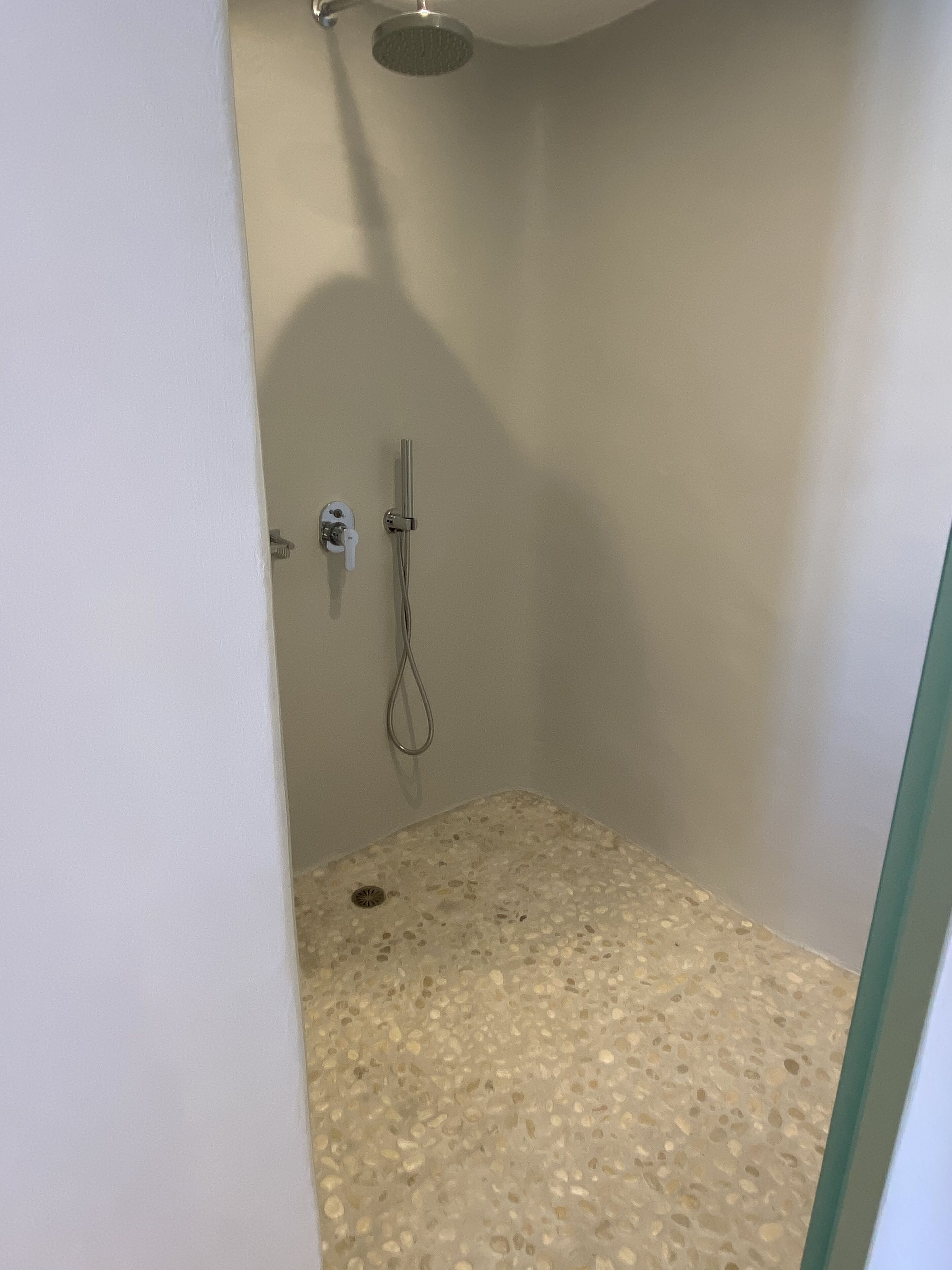 Pequeño espacio de ducha cerrado con piso de baldosas y ducha de mano.