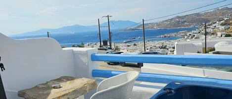 A balcony with a hot tub, white wicker chairs, and a view of the sea and distant mountains.