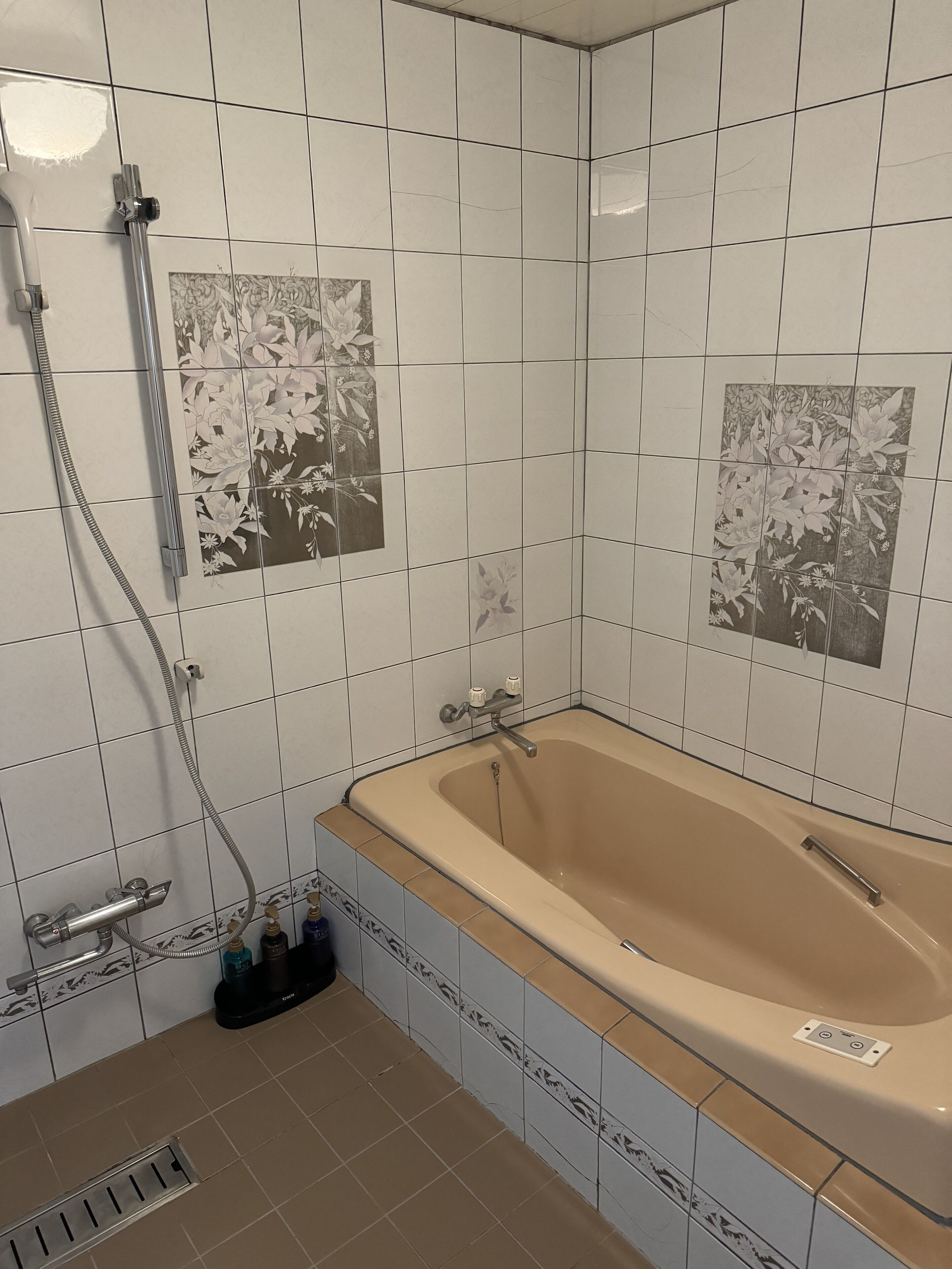 Un baño con bañera, ducha y paredes de azulejos con motivos florales.