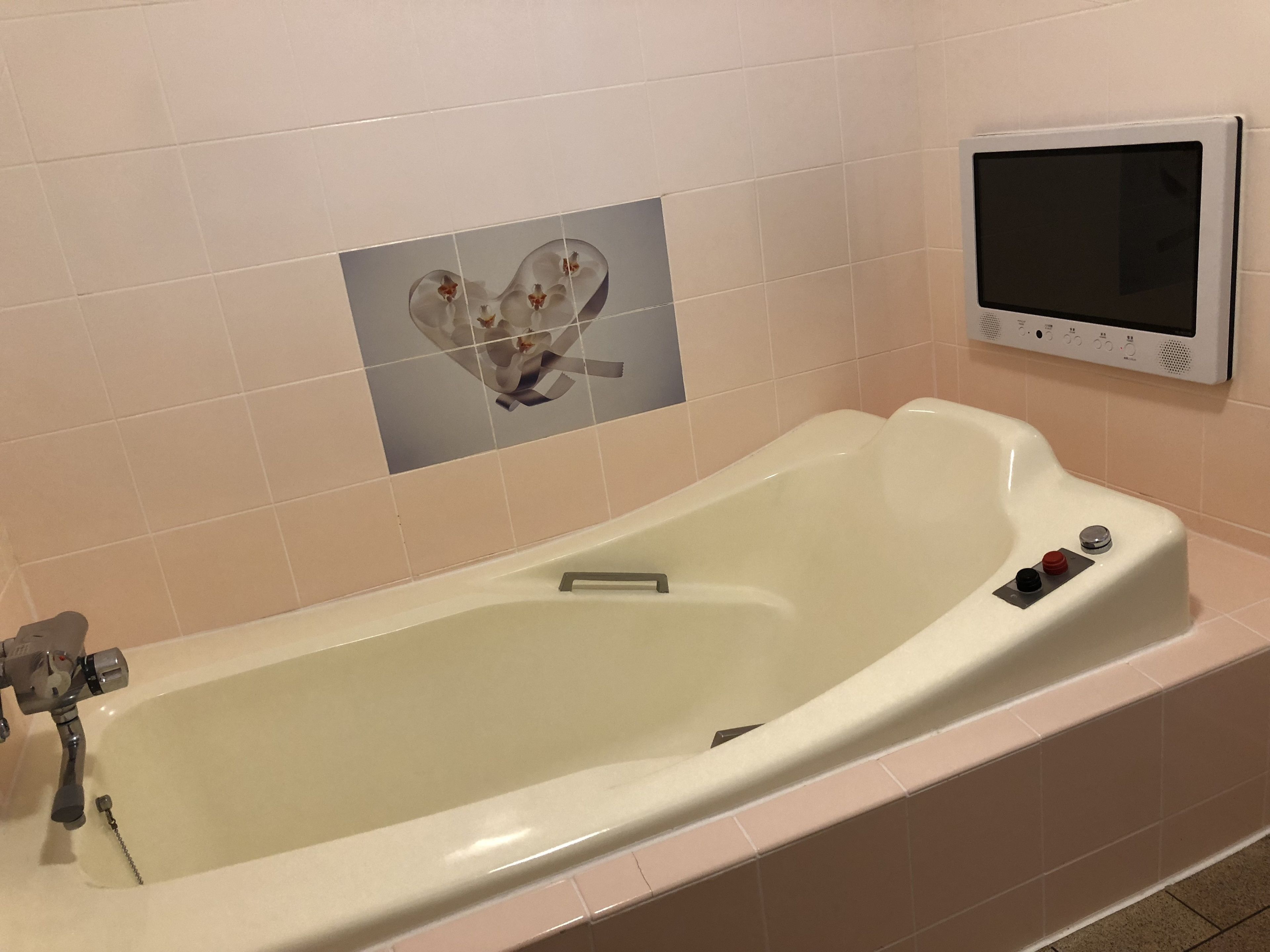 A bathtub with a control panel, a heart-shaped tile decoration, and a thermostat on the wall.