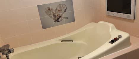 Una bañera con un panel de control, un adorno de azulejo con forma de corazón y un termostato en la pared.