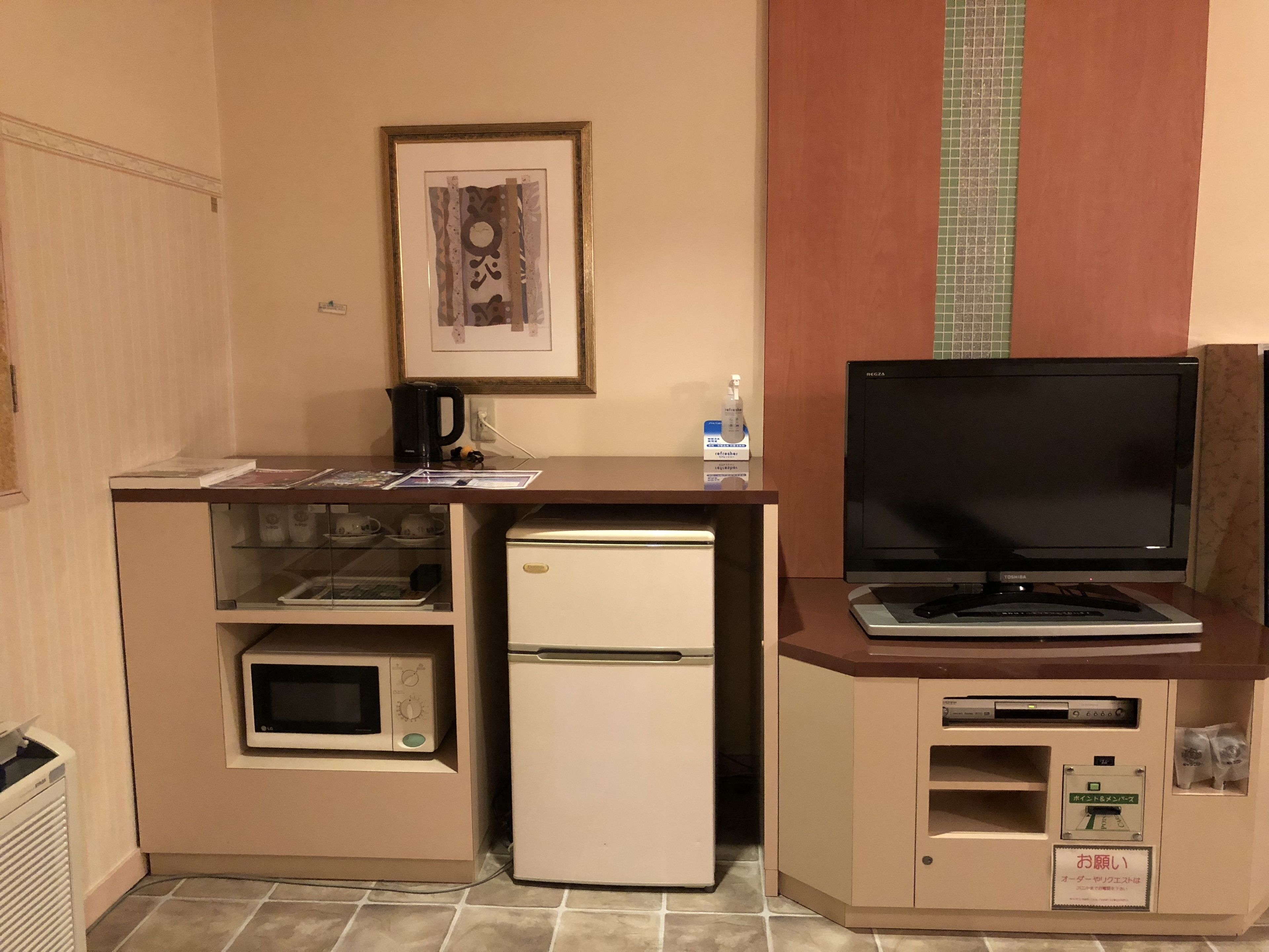 A compact kitchenette with a microwave, refrigerator, and a small TV on a cabinet.