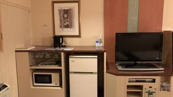 A compact kitchenette with a microwave, refrigerator, and a small TV on a cabinet.