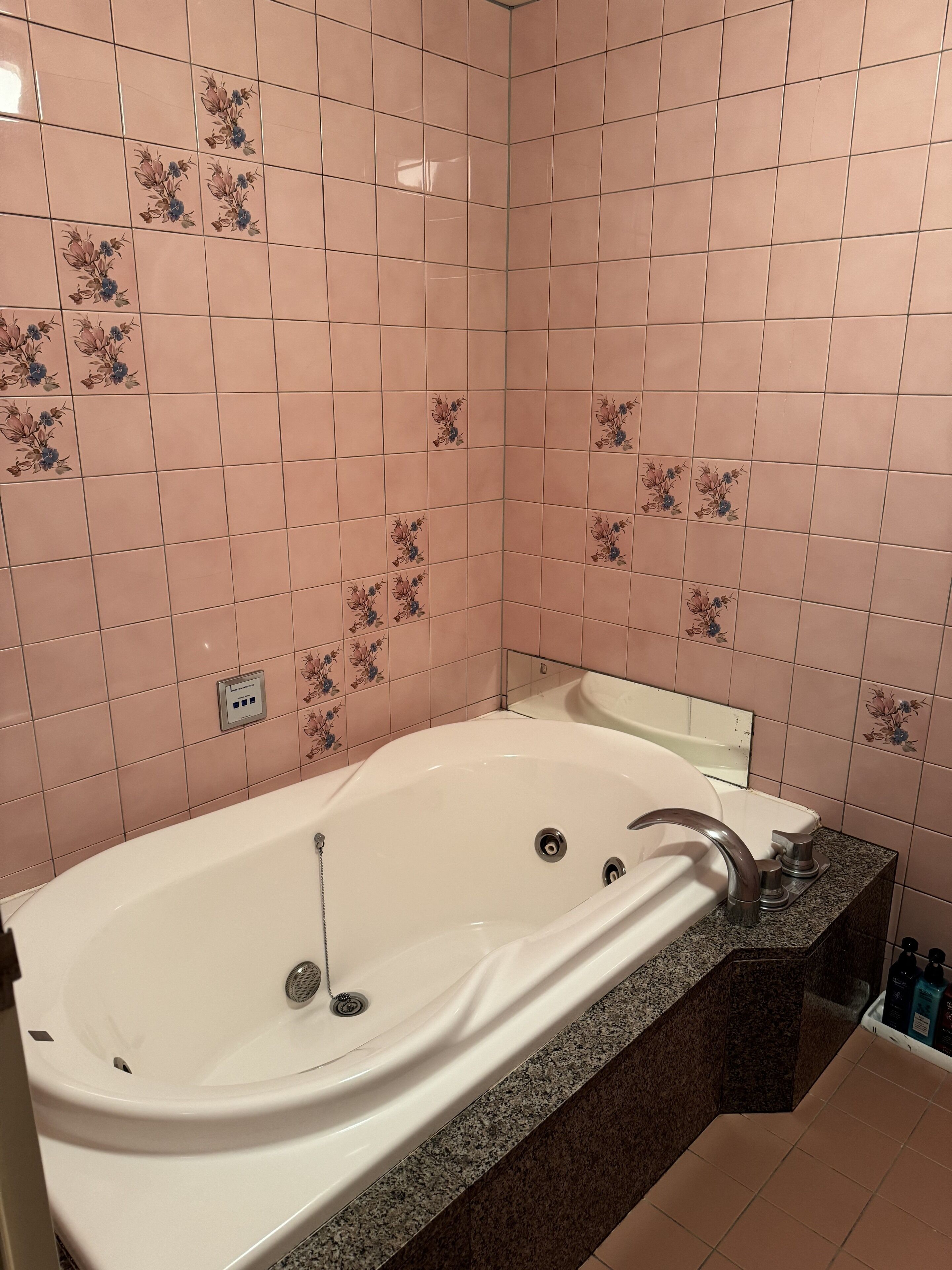 A bathroom with a freestanding bathtub, a granite countertop, and pink floral tiles on the walls.