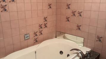 A bathroom with a freestanding bathtub, a granite countertop, and pink floral tiles on the walls.