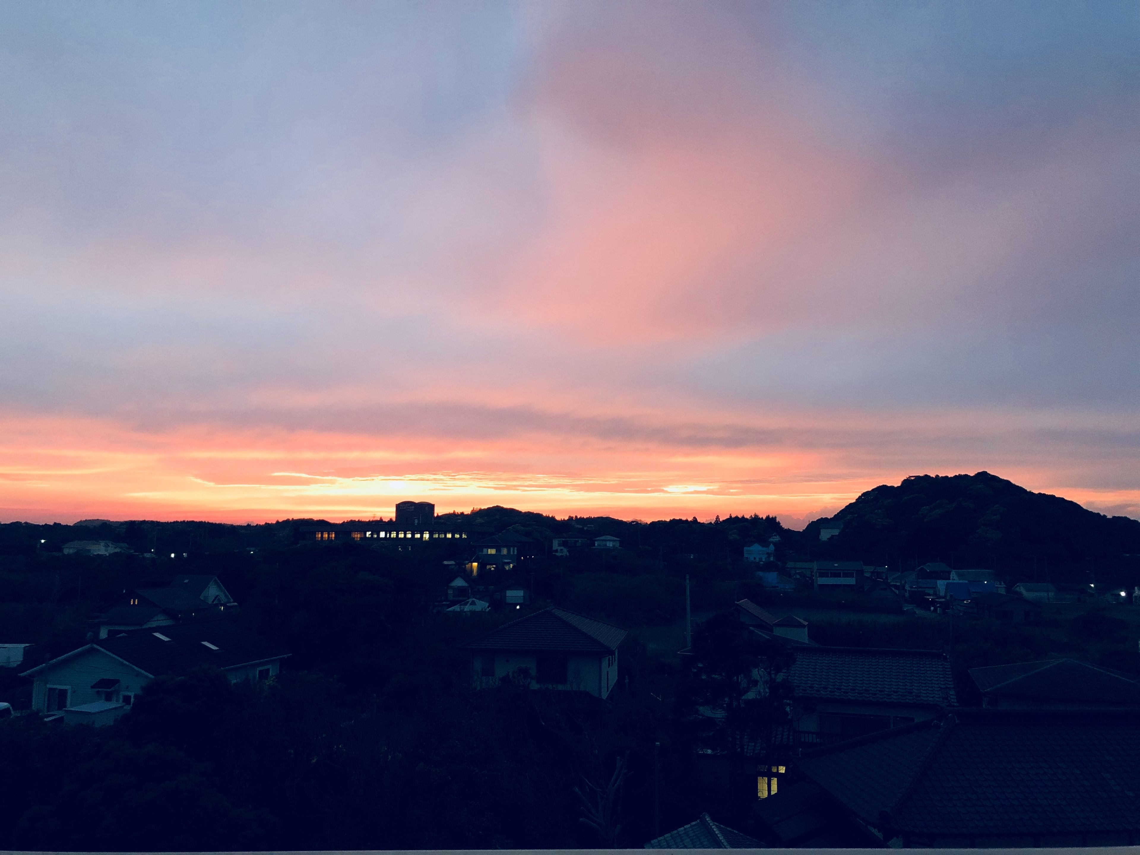 Een zonsondergang boven een woonwijk met huizen en een heuvel op de achtergrond.