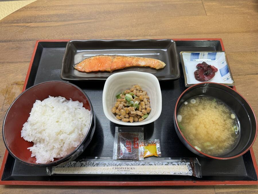 Una bandeja con arroz blanco, un tazón de sopa de miso, un plato de vegetales encurtidos y un trozo de salmón.