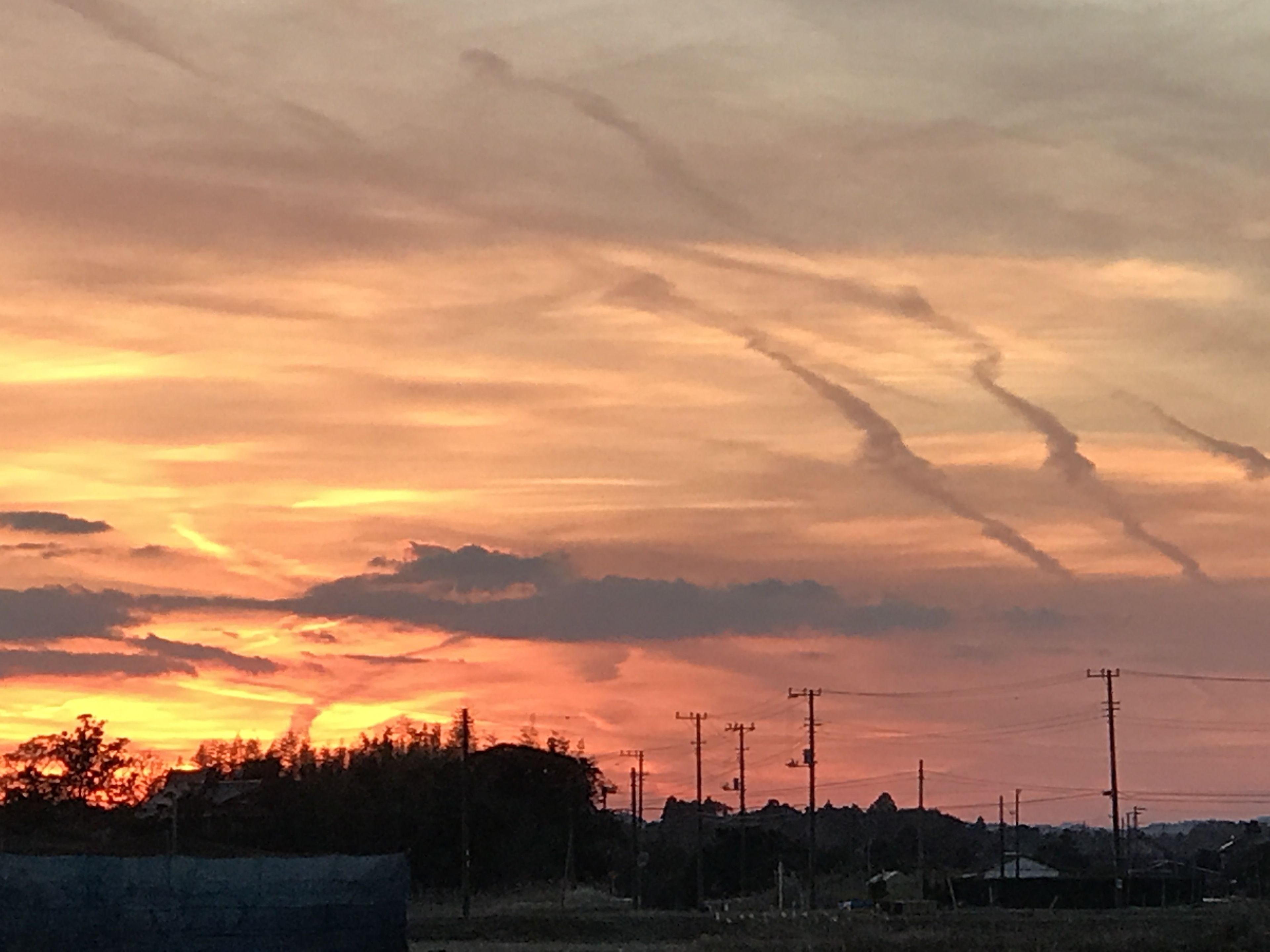 Ein Sonnenuntergang über einer ländlichen Landschaft mit Bäumen und Stromleitungen.