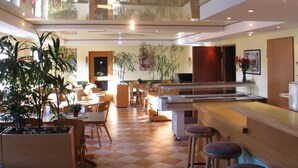 A spacious hotel lobby with a checkered floor, multiple seating areas, and a variety of plants. - Hotel Vitalesca (Neuschoenau)