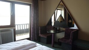 A hotel room with a bed, a small table, two chairs, a mirror, and a window with curtains. - Hotel Vitalesca (Neuschoenau)