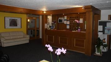 Un espace d’accueil avec un bureau en bois, un canapé beige et un vase rempli de fleurs roses.