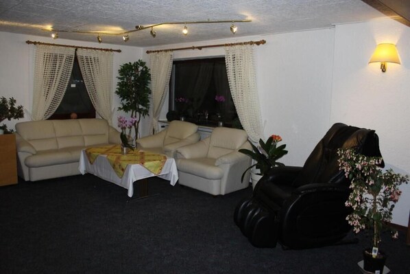 Una sala de estar con un sofá color beige, un sillón de cuero negro, una pequeña mesa con mantel amarillo y una planta en maceta.