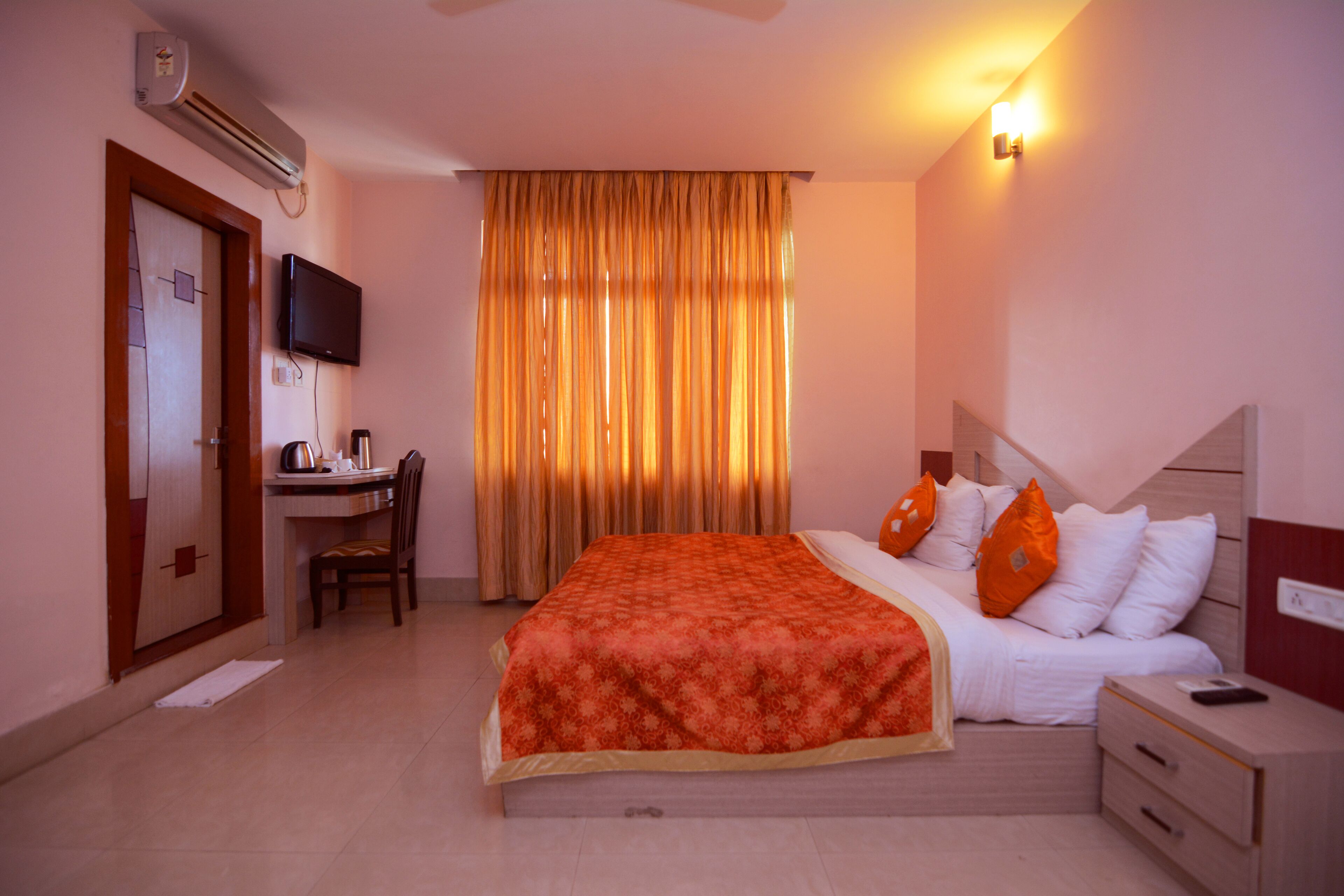 Habitación de hotel con cama, escritorio, silla, televisor y ventana con cortinas.